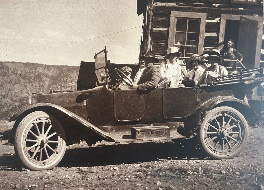 A vintage photograph depicting a vehicle carrying women on a dirt road in Gold Hill.